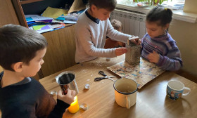 three children sit at a table doing crafts