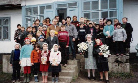 a large group of children standing outdoors on the front steps and porch of a building