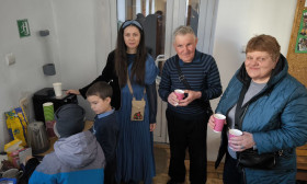 Ukrainian refugees, a woman, two children, and an elderly couple, gather for warm drinks in a temporary shelter.