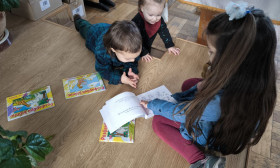 Three young children, two boys and a girl, are engrossed in reading books on a wooden floor, fostering early literacy.