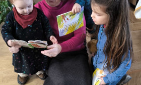 Elderly woman reading engaging children's books to three diverse young kids, fostering early literacy and family bonding.