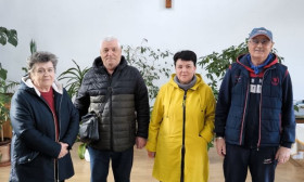 Four elderly people stand in a church, each with a bag of humanitarian aid, symbolizing community support and charity.