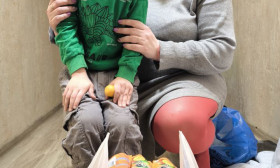 Happy mother and child with a bag of humanitarian aid, including baby food and hygiene products, in a hallway.