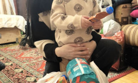 Mother and child with a bag of humanitarian aid, including diapers and baby food, in a home setting.