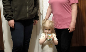 Three Ukrainian women, one in military uniform, receiving humanitarian aid bags. A child holds a juice box.