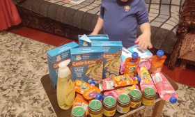 A young boy stands over a table filled with various baby food products, including cereals, purees, and snacks.
