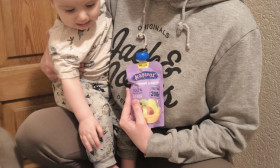 Happy mother and baby with a bag of baby food and supplies, including fruit puree, supporting child nutrition.